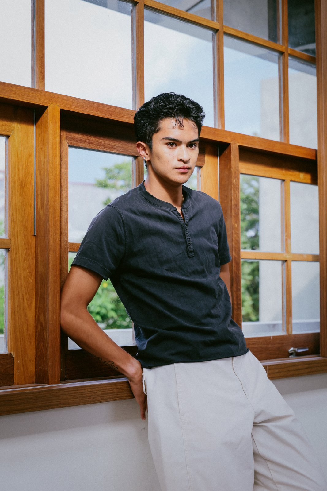 Ratanon in a navy henley, leaning against a wooden window