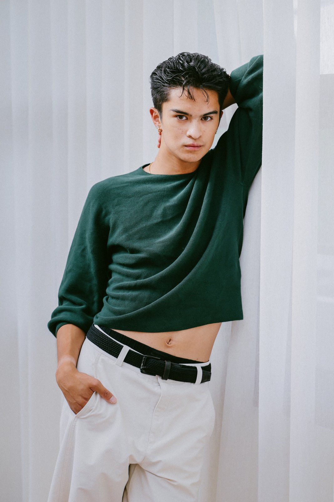 Ratanon in a cropped green sweater against sheer curtains