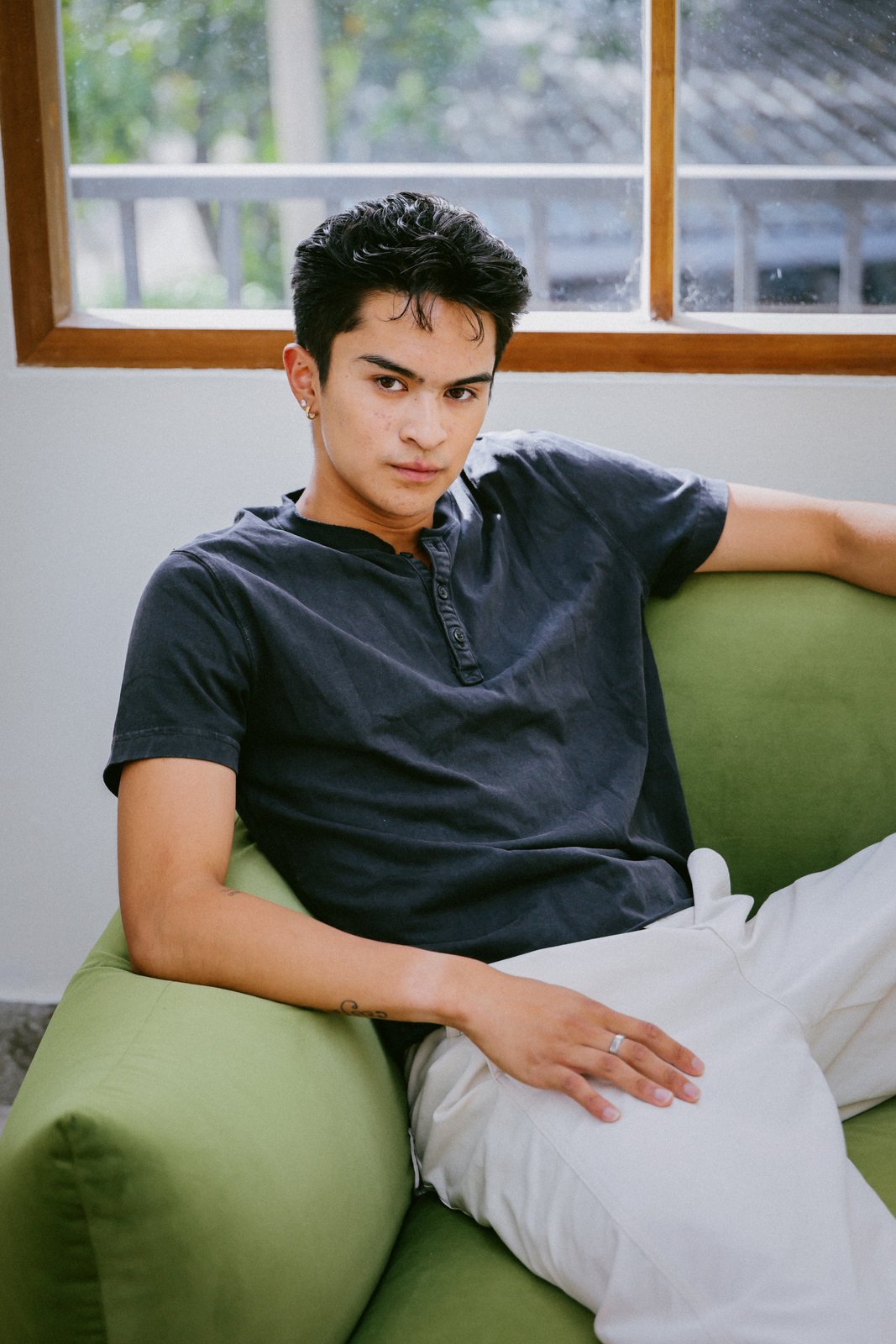 Ratanon in a navy henley, seated on a green sofa