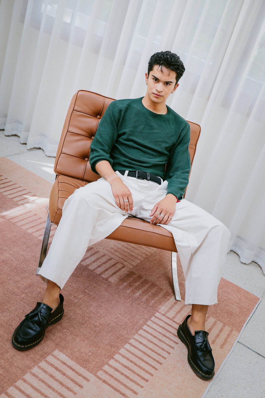 Ratanon in a green sweater, seated in a leather chair, alternate pose