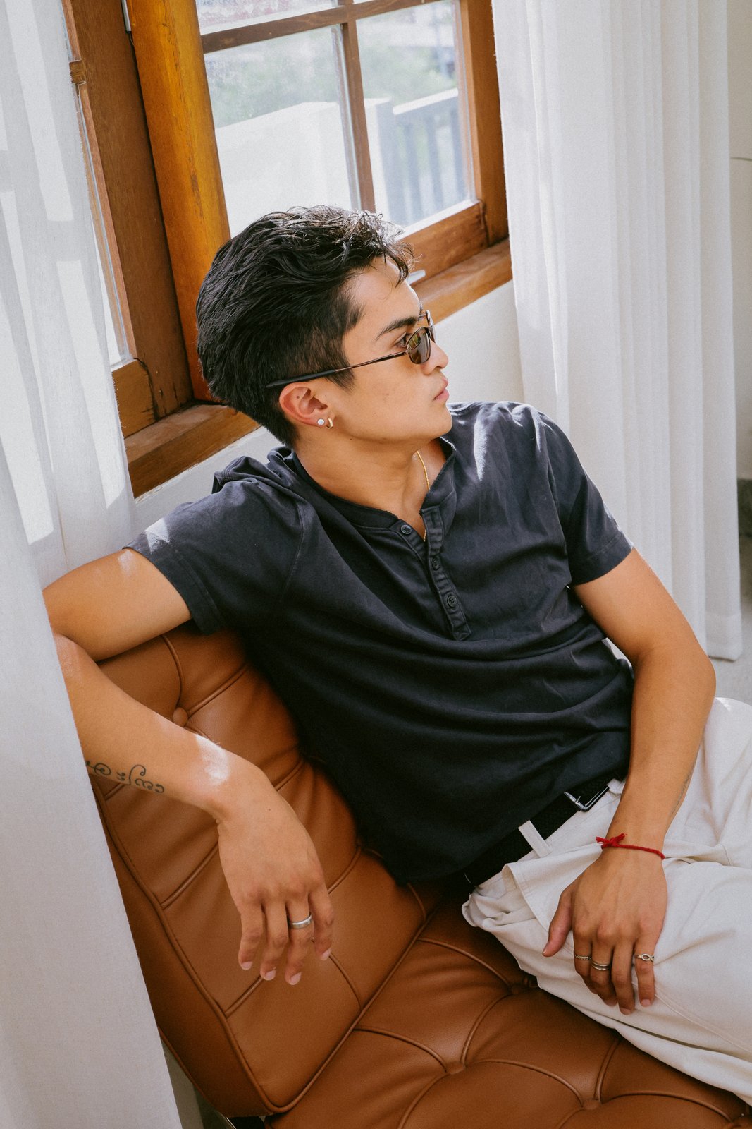 Ratanon in sunglasses, seated on a leather sofa, alternate pose