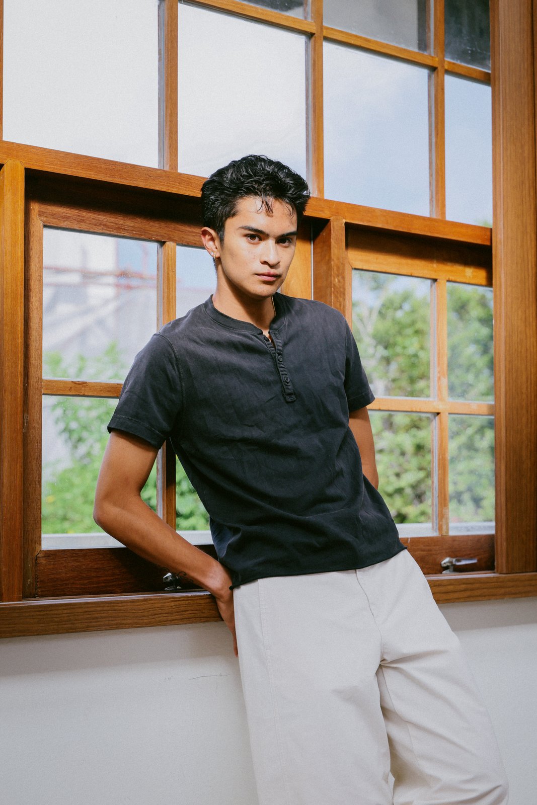 Ratanon in a navy henley, portrait by a wooden window, alternate pose