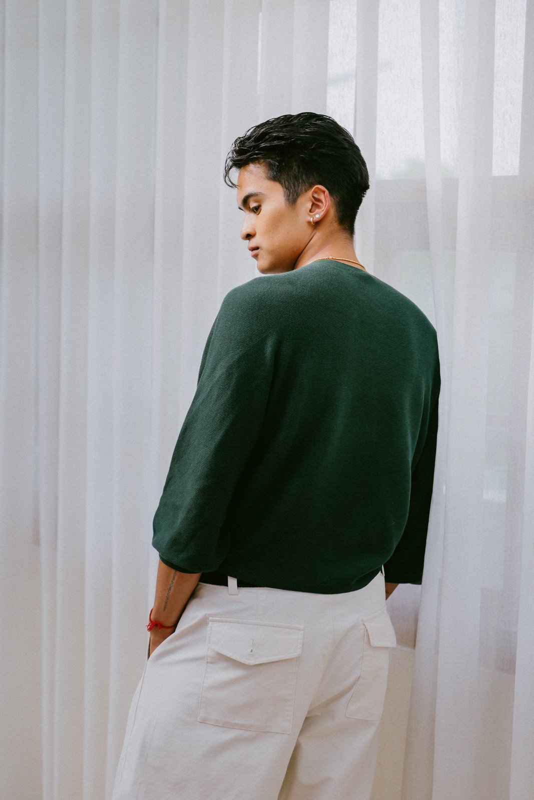 Ratanon in a green sweater, back view against sheer curtains